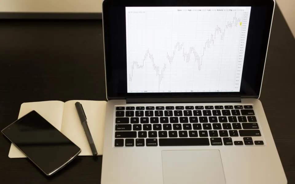 A laptop showing a live line chart on a dark desk with a notebook and phone.