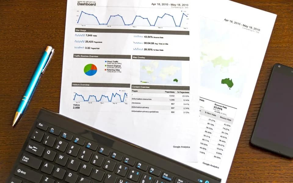 Printed reports, a pen and a keyboard on a wooden desk.