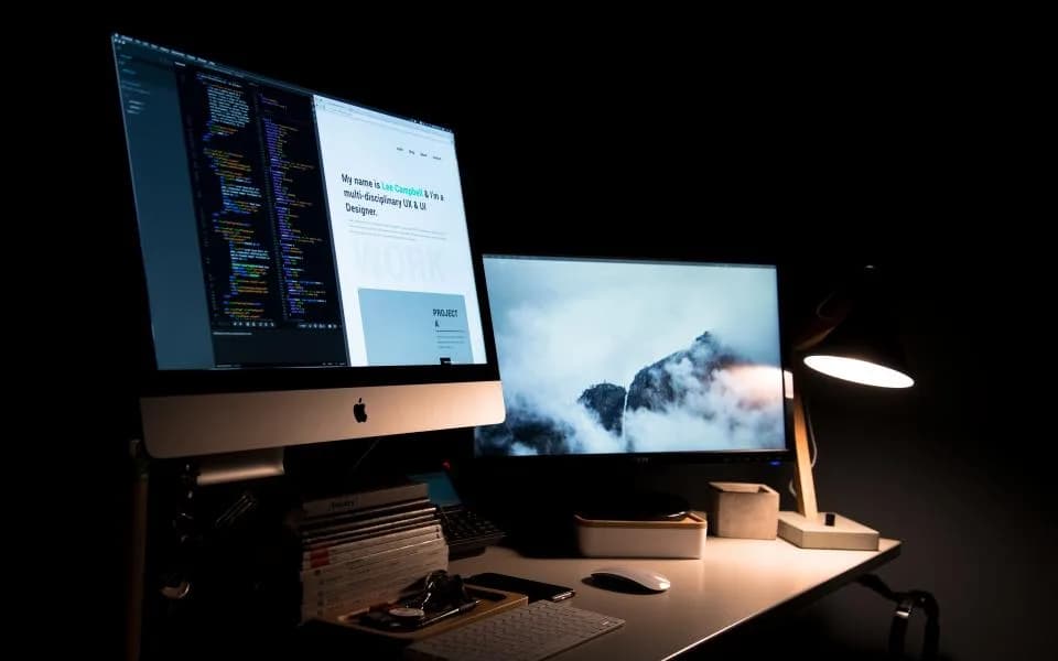 A dual-monitor workstation at night with code and a dashboard on screen.
